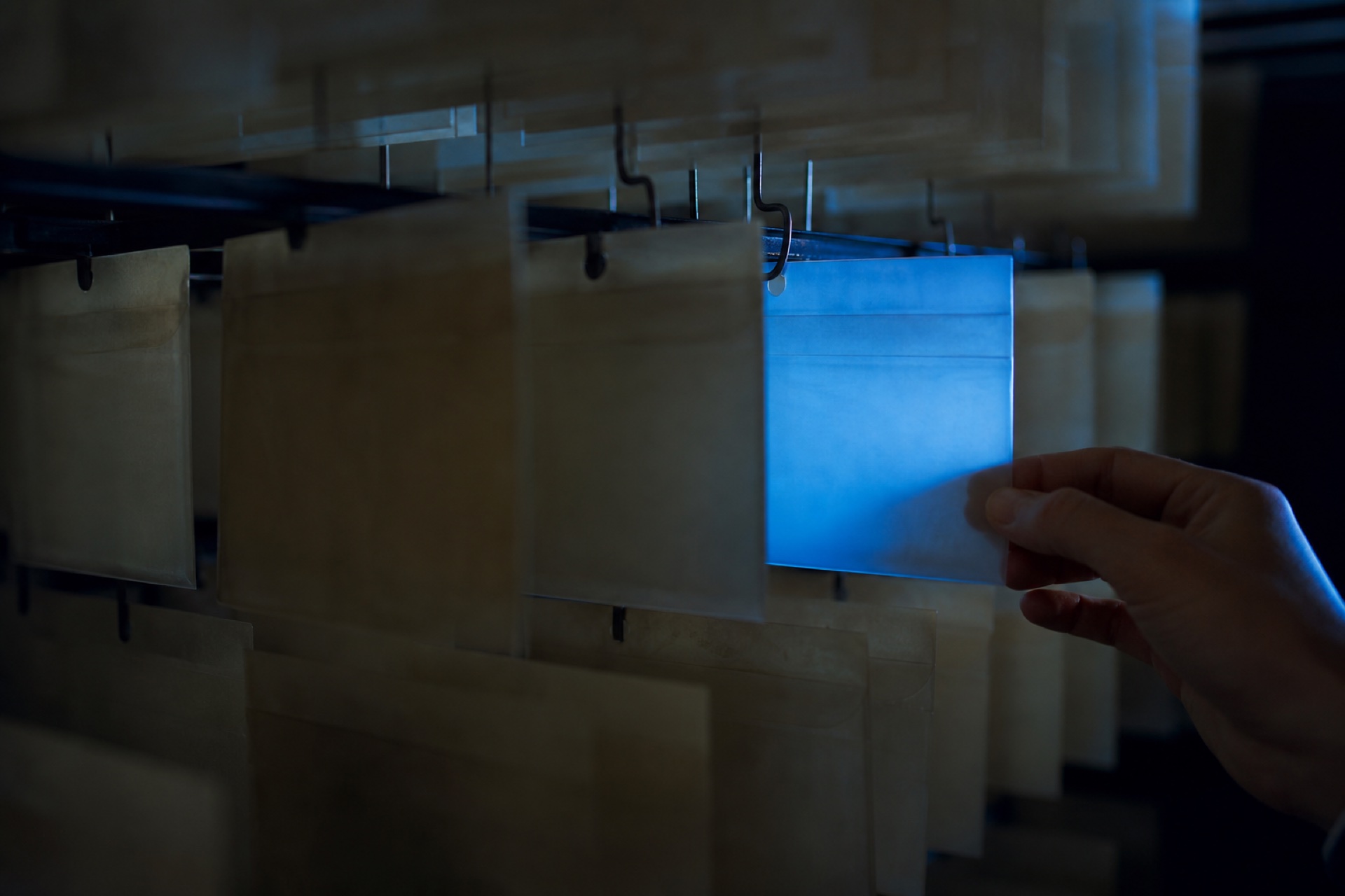 A hand selecting one cobalt-lit card from a dark physical archive